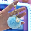 Detail of light blue faux rabbit fur pom pom keychain with a large white pearl and gold clasp - Blue