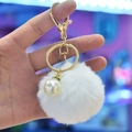 Detailed view of white faux rabbit fur pom pom keychain with gold clasp and pearl charm - White