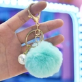 Macro detail of mint green faux fur ball keychain with white pearl and gold metal ring - Green