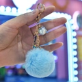 Close-up of blue faux fur pompom keychain with golden heart clasp and miniature charms - Blue