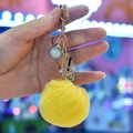 Detail of yellow faux fur pom pom keychain with gold heart clasp and mini drink charm - Yellow