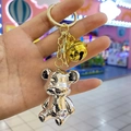 Gros plan d'un porte-clés ours en métal argenté avec une clochette dorée tenu à la main - Boucle en Or Clair + Ours + Cloche / Blanc