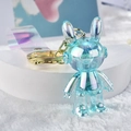 Iridescent blue acrylic bunny keychain with gold metal ring on white podium - Blue
