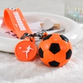 Dettaglio ravvicinato di un portachiavi da calcio arancione con pallone in PVC e cinturino - Stile Cordino / Arancione