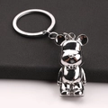 Polished silver metal bear keychain with bow tie detail on a textured leather background - Silver