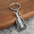 Dettaglio di un portachiavi a chitarra argentato con strass neri su base di legno - Zircone Nero