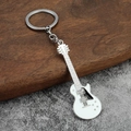 Dettaglio del portachiavi a forma di chitarra elettrica bianca su sfondo di legno e roccia - Bianco