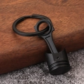 Close-up of matte black metal engine piston keychain on a textured wooden block - Black with Hook