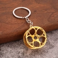 Detail of a golden five-spoke car wheel rim keychain with a polished silver ring - Gold