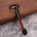 Detail shot of a black shock absorber keychain with a red spring on a stone surface - Red