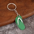 Detail of green flip-flop keychain with silver metal strap on a stone and wood surface - Green