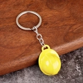 Close-up of a mini yellow safety helmet keychain with metal ring on a textured surface - Yellow