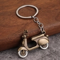 Macro detail of a vintage bronze scooter keychain on a rustic wood and stone background - Antique Bronze Scooter