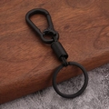 Close-up of a matte black metal spring keychain with carabiner on industrial background - Black
