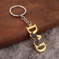 Close-up of golden metal DAD keychain featuring black mustache detail on wood background - Gold Mustache DAD