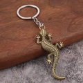Vintage bronze gecko keychain with detailed lizard scale texture on rustic wood and stone - Bronze
