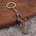 Vintage gecko keychain with copper-toned lizard scales on a rustic wood and stone background - Antique Red