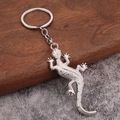 Detailed macro shot of silver gecko keychain with realistic textures on wood and stone - White K/Silver