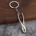 Detailed close-up of a silver metal plier-shaped keychain on a wooden surface - Pliers