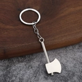 Close-up of a silver axe-shaped metal keychain on a wood and stone background - Axe