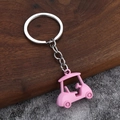 3D pink metal golf cart keychain with silver ring on dark wood and grey ground - Pink