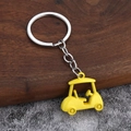 Macro view of bright yellow 3D golf cart keychain with silver ring on wooden surface - Yellow