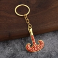 Détail d'un porte-clés doré en forme de hache avec émail rouge sur socle en bois - Bouilloire Ethnique
