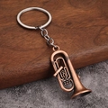Detalle de llavero de tuba en cobre vintage con acabado antiguo sobre mesa de madera - Estilo A (Tuba/Bombardino) - Rojo Antiguo