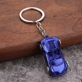 Close-up of a blue metal sports car keychain with silver wheels on a textured surface - Blue