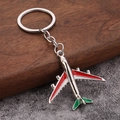 Metal airplane keychain with red, white, and green finish on wooden surface - Red White