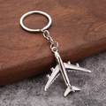 Detail view of a silver airplane keychain with white wings on a dark wood background - White