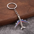 Detailed close-up of a silver airplane keychain with blue and red enamel on wood background - Blue Red