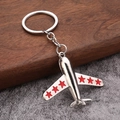 Polished silver metal airplane keychain with red stars on wings over wooden display - Red