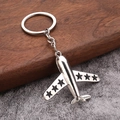 Silver metal aircraft keychain with star wings on dark wooden and stone background - Black