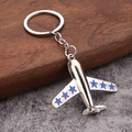 Close-up of silver metal airplane keychain with blue star detail on wing and round ring - Blue