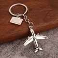 Polished silver metal airplane and suitcase keychain on a textured stone and wood background - Bright Silver (White K)