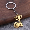 Detail eines goldenen Fußball- und Pokal-Schlüsselanhängers auf einem Holzsockel - Gold