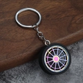 Colorful metal alloy car wheel hub keychain with black rubber tire on textured background - Iridescent