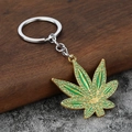 Llavero de hoja de arce dorada estilo hip hop con cristales verdes sobre fondo piedra - Oro + Diamante de Imitación Verde