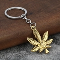 Minimalist golden maple leaf keychain with silver ring on a rustic wood and stone background - Gold