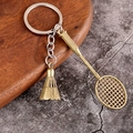 Llavero de raqueta de bádminton y volante en metal bronce sobre fondo de madera - Bronce