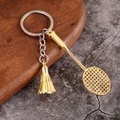Llavero creativo de metal con raqueta de bádminton dorada y volante sobre madera - Dorado