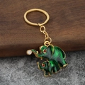 Portachiavi con elefante dorato in smalto verde e perla bianca su sfondo legno scuro - Verde