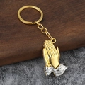 Golden and silver praying hands keychain on wooden and stone background - Gold Palm Silver Cuff (Imitation Gold)