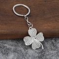 Detailansicht silberner Kleeblatt-Schlüsselanhänger mit Strass auf Holz und Stein - Silber Weißer Strass