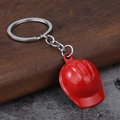 Close-up of a miniature red safety helmet keychain on a rustic wooden and stone background - Red