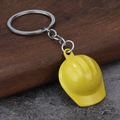 Close-up of a bright yellow construction safety helmet keychain on a wooden stand - Yellow