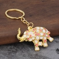 Detail of golden elephant keychain with colorful drip oil polka dots on walnut wood surface - Pink