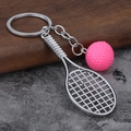 Detail van roze tennisbal en zilveren racket sleutelhanger op hout en steen - Roze