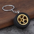 Detail eines Autoreifen Schlüsselanhängers mit schwarzem Gummirad und goldener Felge auf Textur - Gold